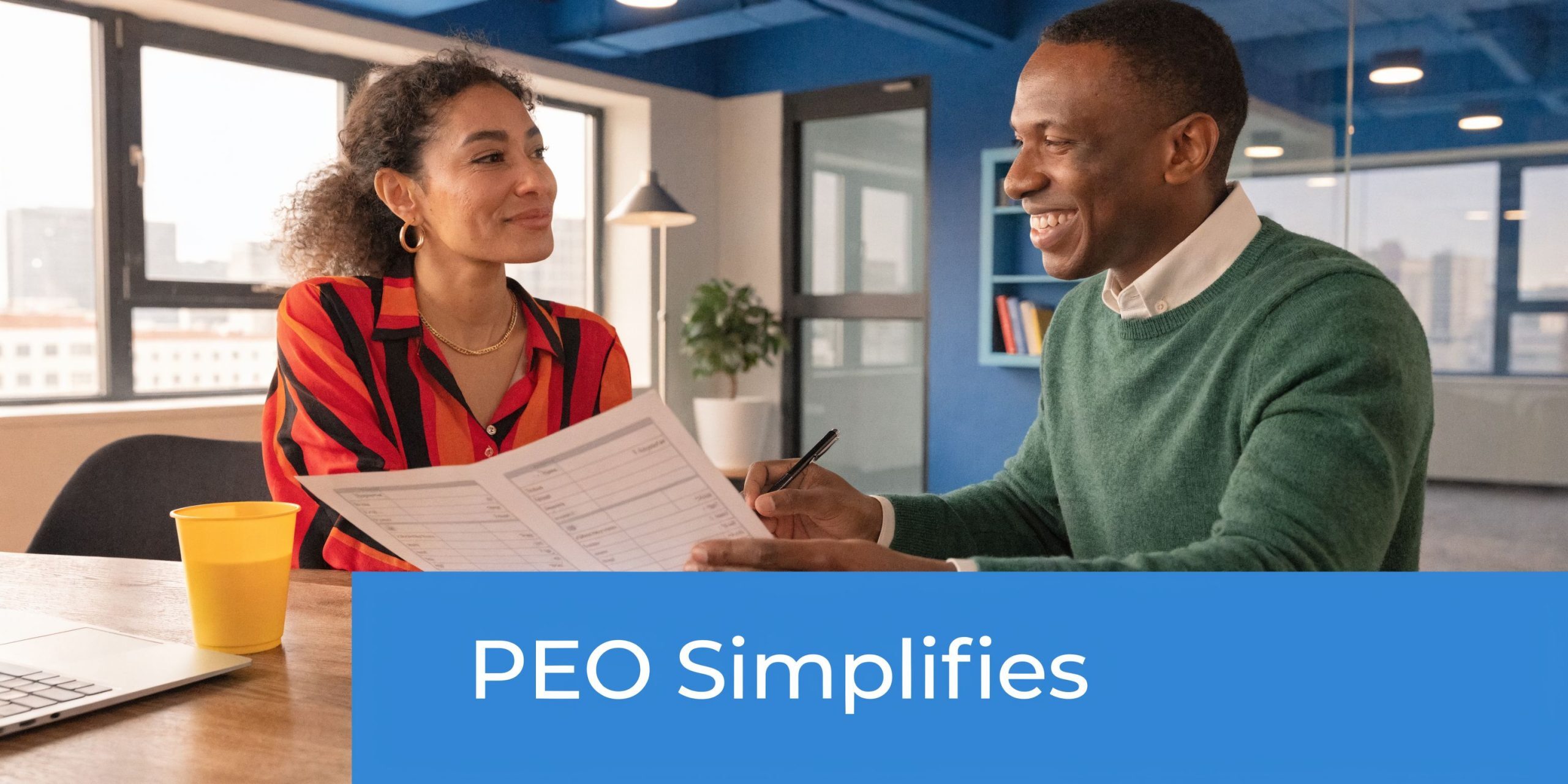 A professional man and woman smiling while reviewing a document together in a modern office workspace.