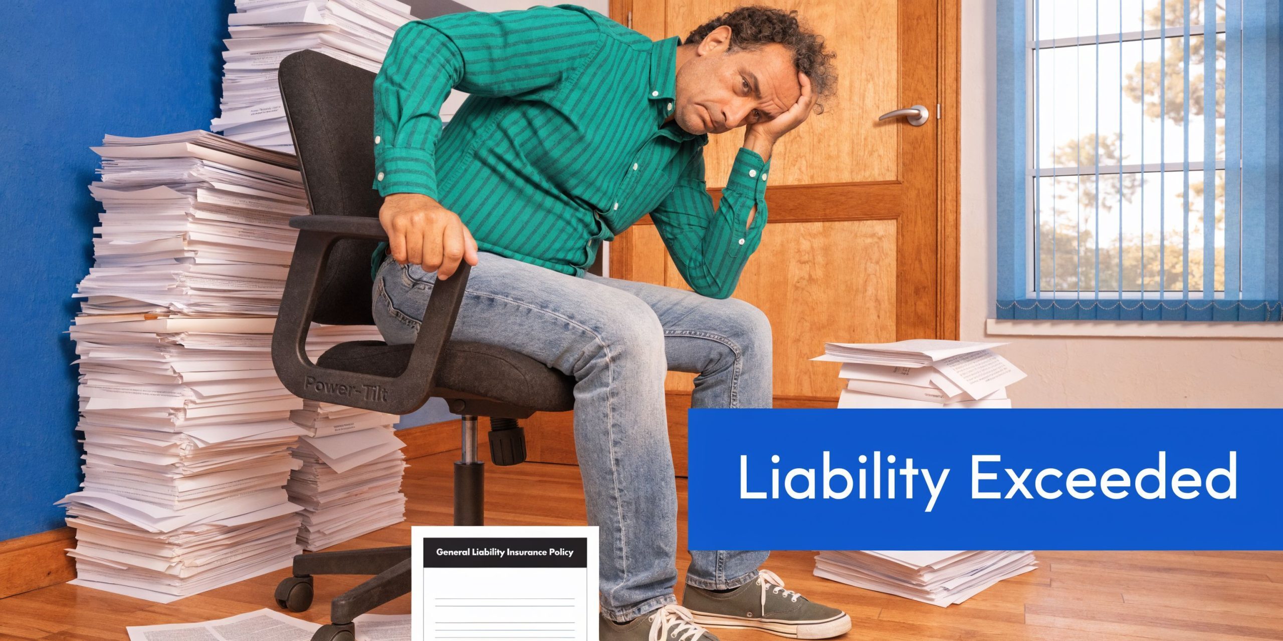 A man looking stressed while sitting in an office surrounded by massive stacks of paper documents.