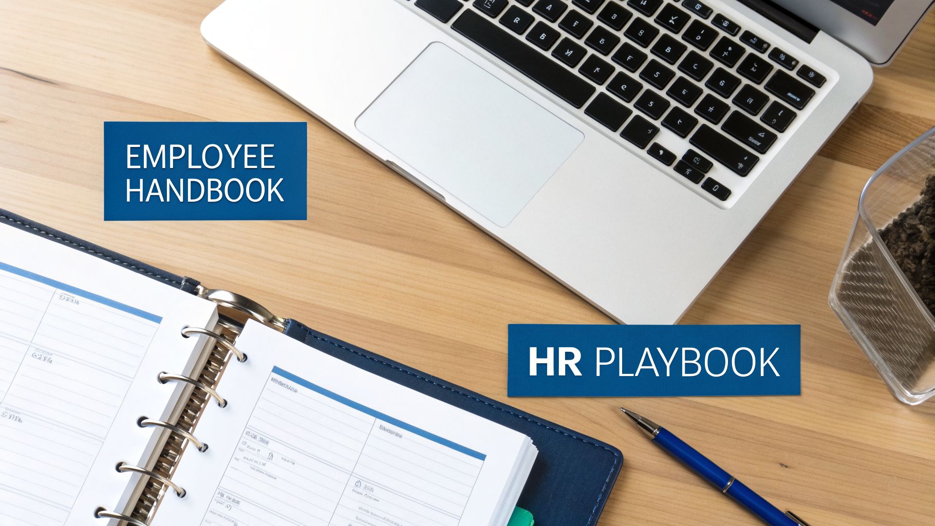 Overhead view of a desk with a laptop, open binder, pen, and labels for Employee Handbook and HR Playbook.
